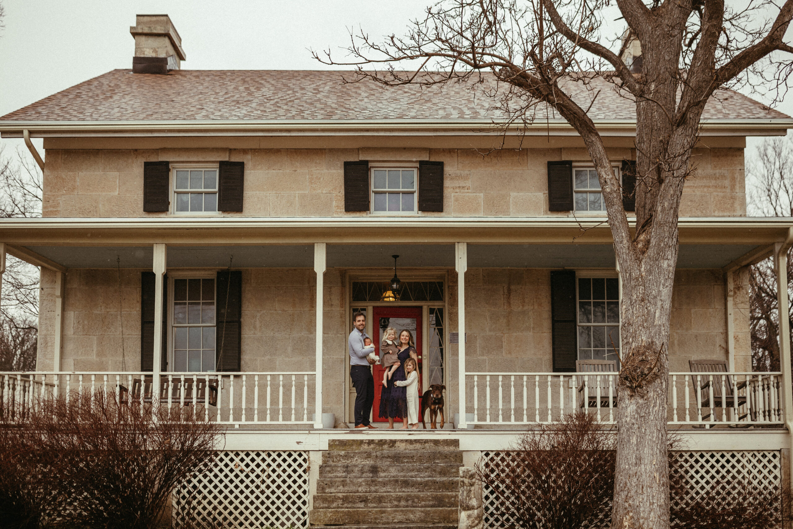 a family of 5 and their dog stands in front of their historical home